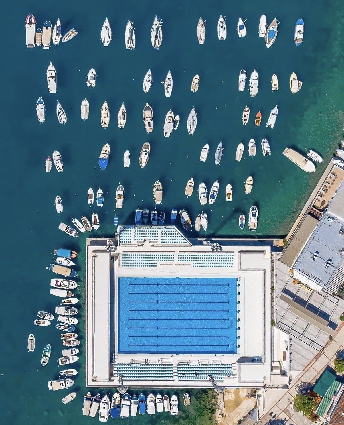 Aerial view of Herceg Novi's open-water pool complex ringed by moored boats